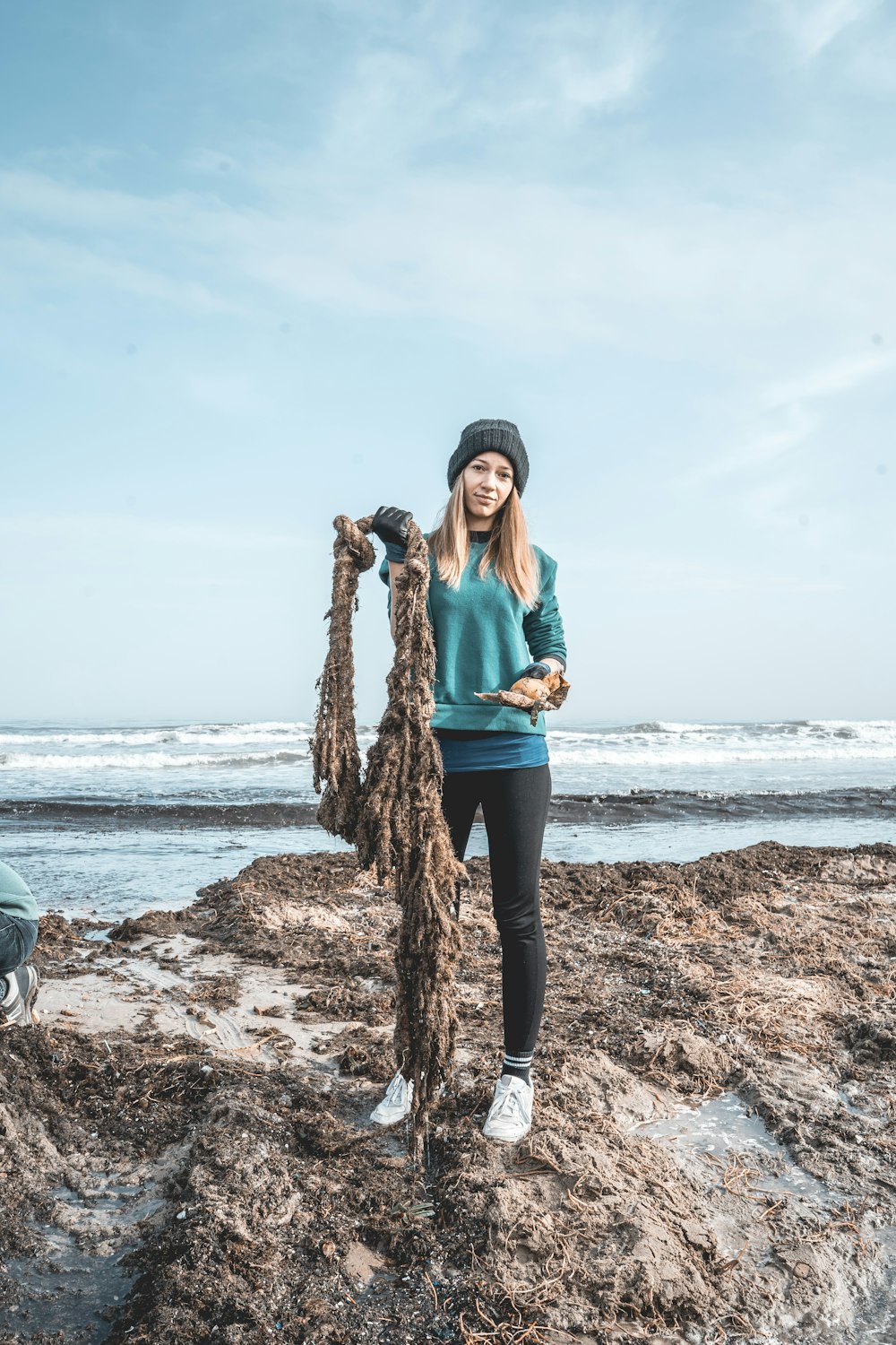 woman in teal long sleeve shirt and black pants standing on brown tree trunk near sea