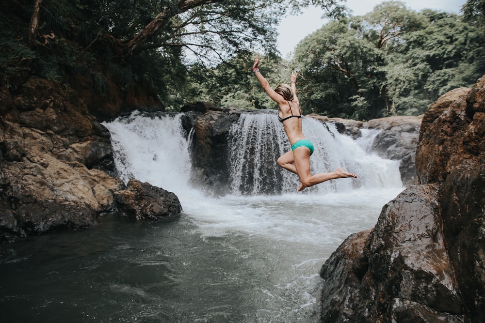 Frau im blauen Bikini springt auf Wasserfälle