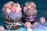 Two elaborately decorated cakes with purple icing and pastel-colored meringues and macarons. Both cakes are wrapped with festive ribbons. The scene is vibrant with a scattering of meringues and macarons on the blue surface.