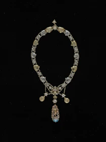 Elegant necklace with intricate gold links and a radiant gemstone centerpiece displayed on a marble surface.