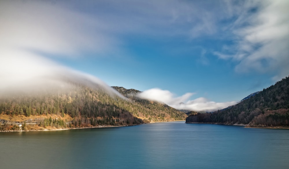 lake near green trees and mountain under blue sky during daytime