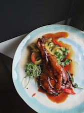 A vibrant photo of a sizzling plate of ginger duck with garnishes on a dark wooden table.
