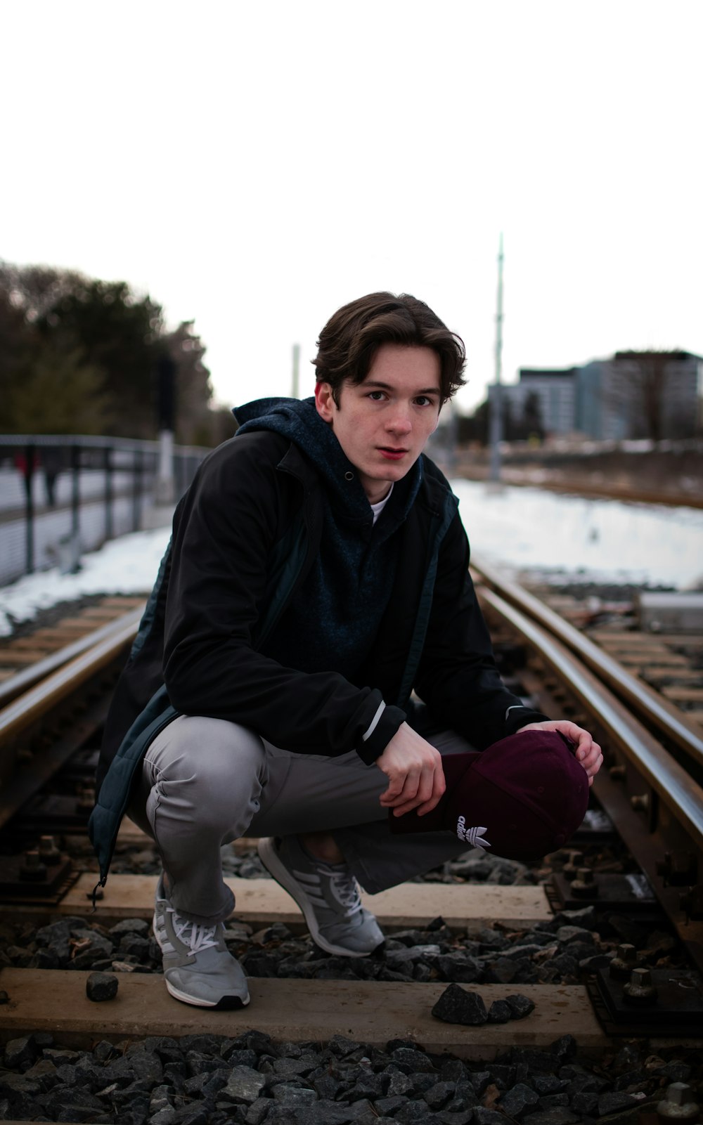 man in black jacket sitting on train rail during daytime