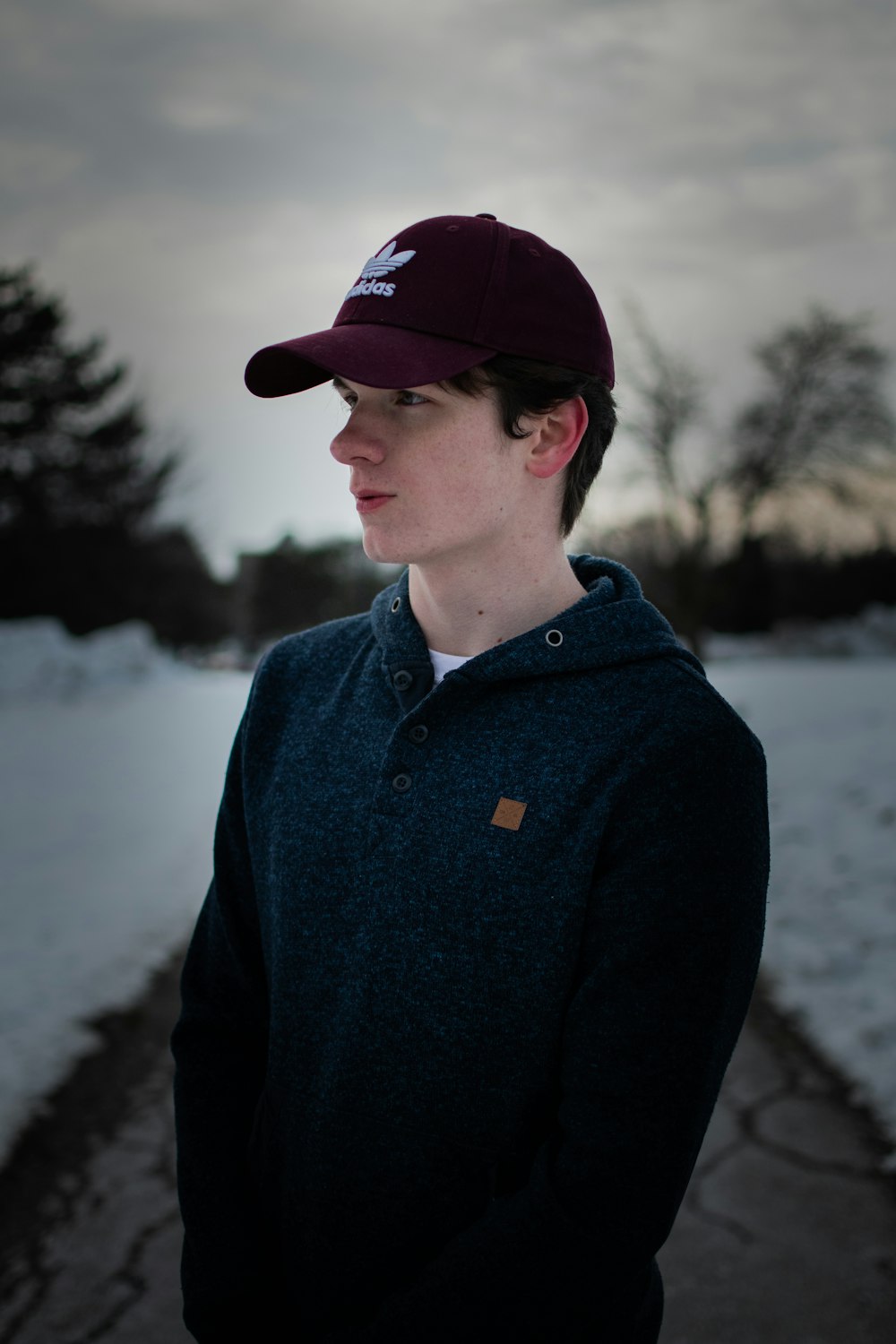 man in blue jacket and red cap standing near lake during daytime