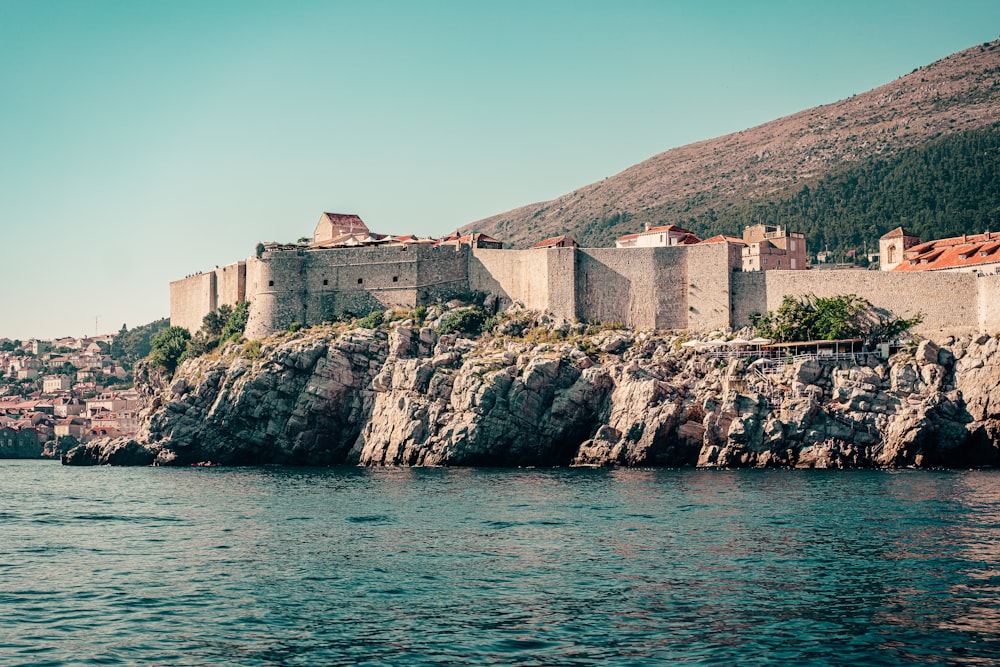 brown concrete building on rock formation near body of water during daytime