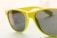 A close-up of a pair of sunglasses with a vibrant yellow-green frame and dark-tinted lenses. The frame has a glossy finish, and the lenses appear almost reflective. The background is softly blurred, focusing attention on the eyewear.