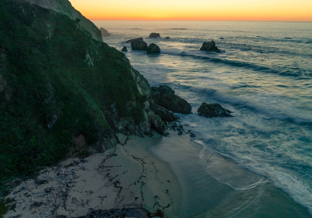 black rock formation on sea shore during sunset