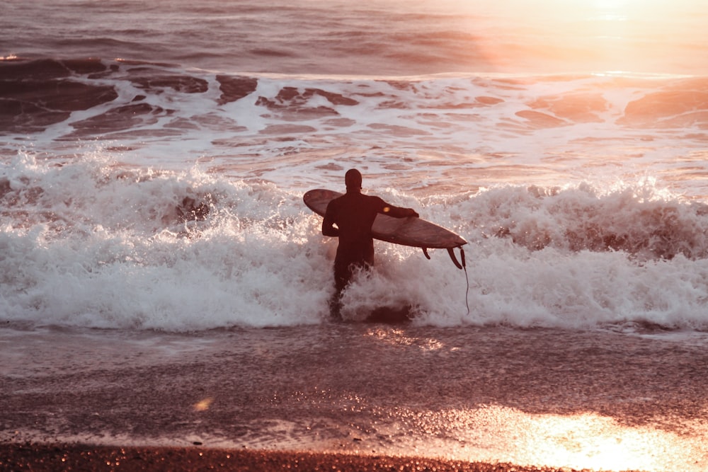 man in black wet suit holding surfboard on beach during daytime