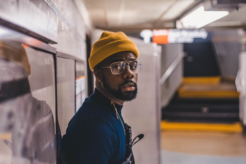 man in blue jacket wearing yellow knit cap and black framed eyeglasses