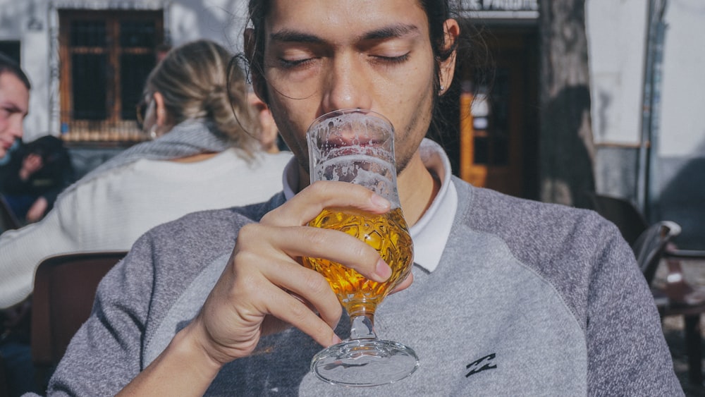 woman in gray sweater holding clear drinking glass