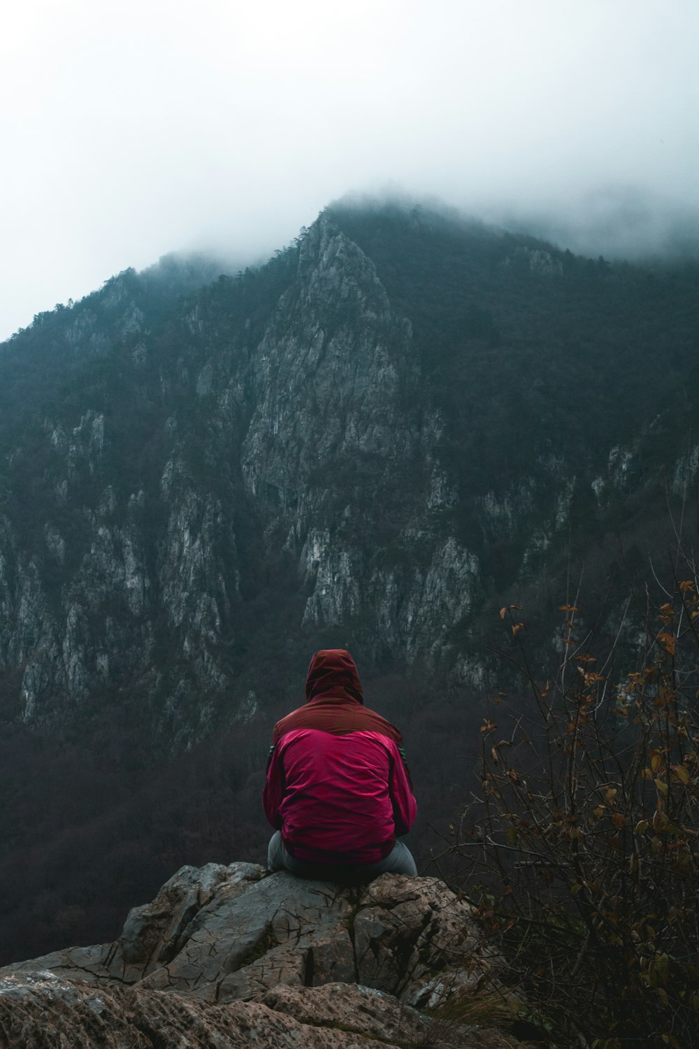 person in red hoodie standing on rocky mountain during daytime