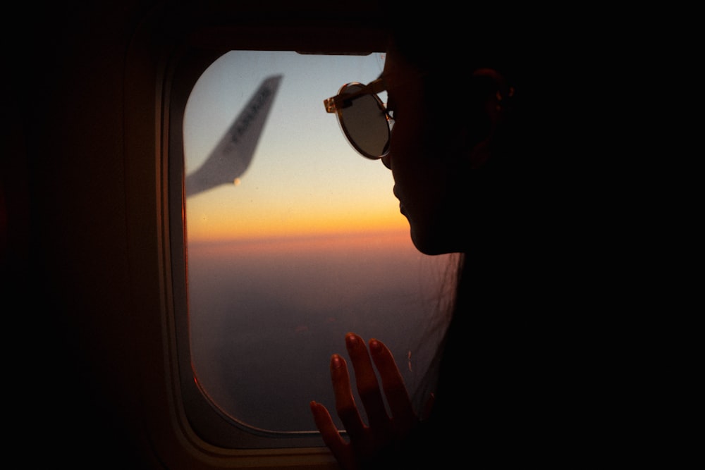 Mann mit schwarzer Sonnenbrille schaut bei Sonnenuntergang ins Flugzeugfenster
