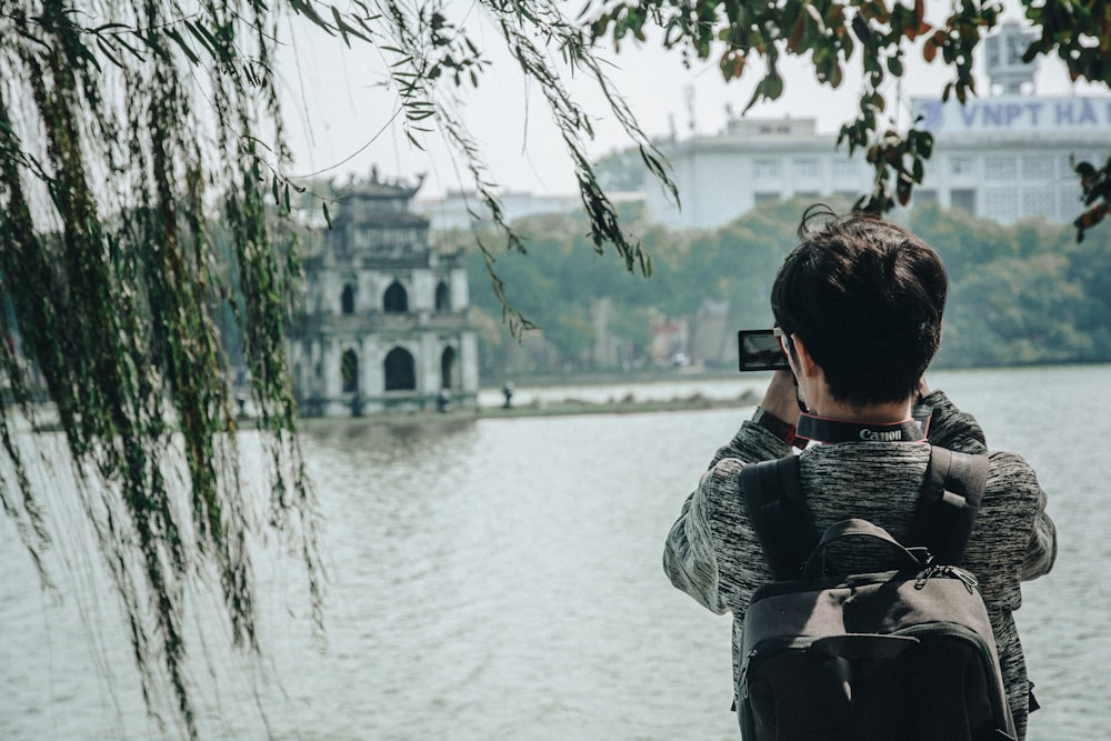 man in black and gray jacket taking photo of white concrete building during daytime