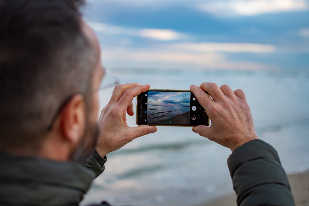 man in gray jacket taking photo of body of water during daytime