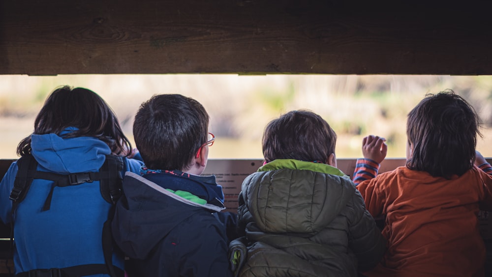 boy in black jacket sitting on brown wooden bench during daytime