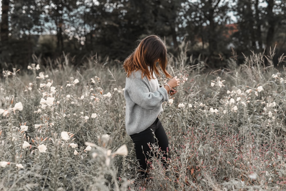 woman in gray sweater and black pants standing on white flower field during daytime