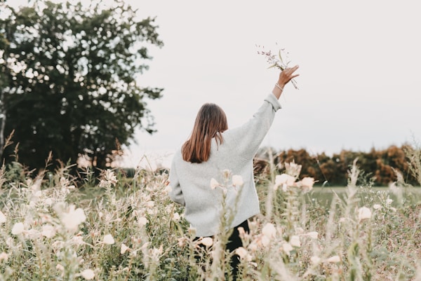 woman in white sweater standing on white flower field during daytimeby Jasmin Ne