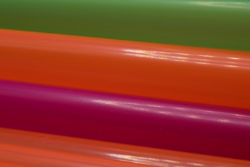 A close-up view of four colorful plastic tubes, arranged in parallel diagonal lines. Each tube has a smooth surface with a shiny finish, reflecting light across its length. The colors are vibrant, offering a visually striking contrast.