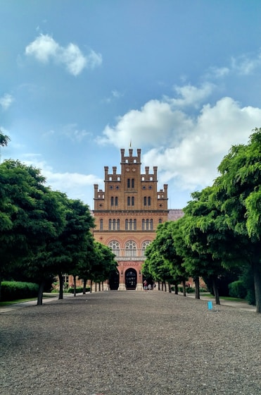 brown concrete building near green trees under white clouds during daytime