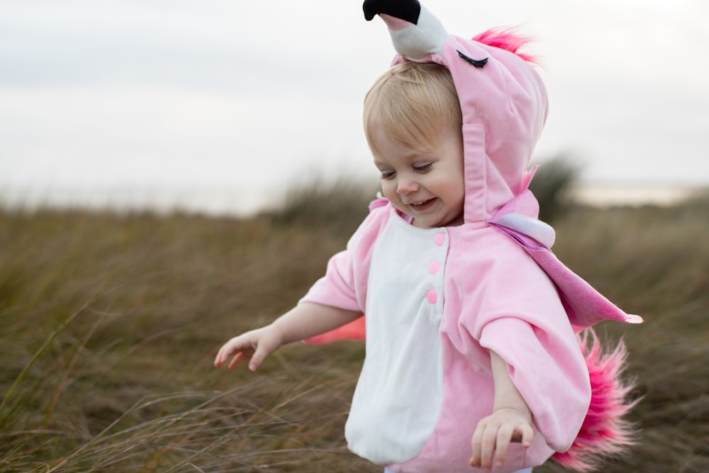 girl in pink hoodie and pink pants sitting on brown grass during daytime