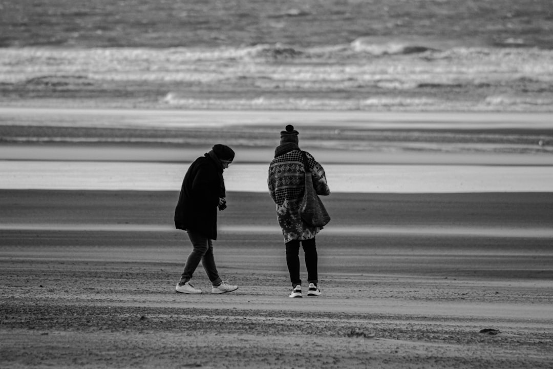 man and woman walking on the beach in grayscale photography
