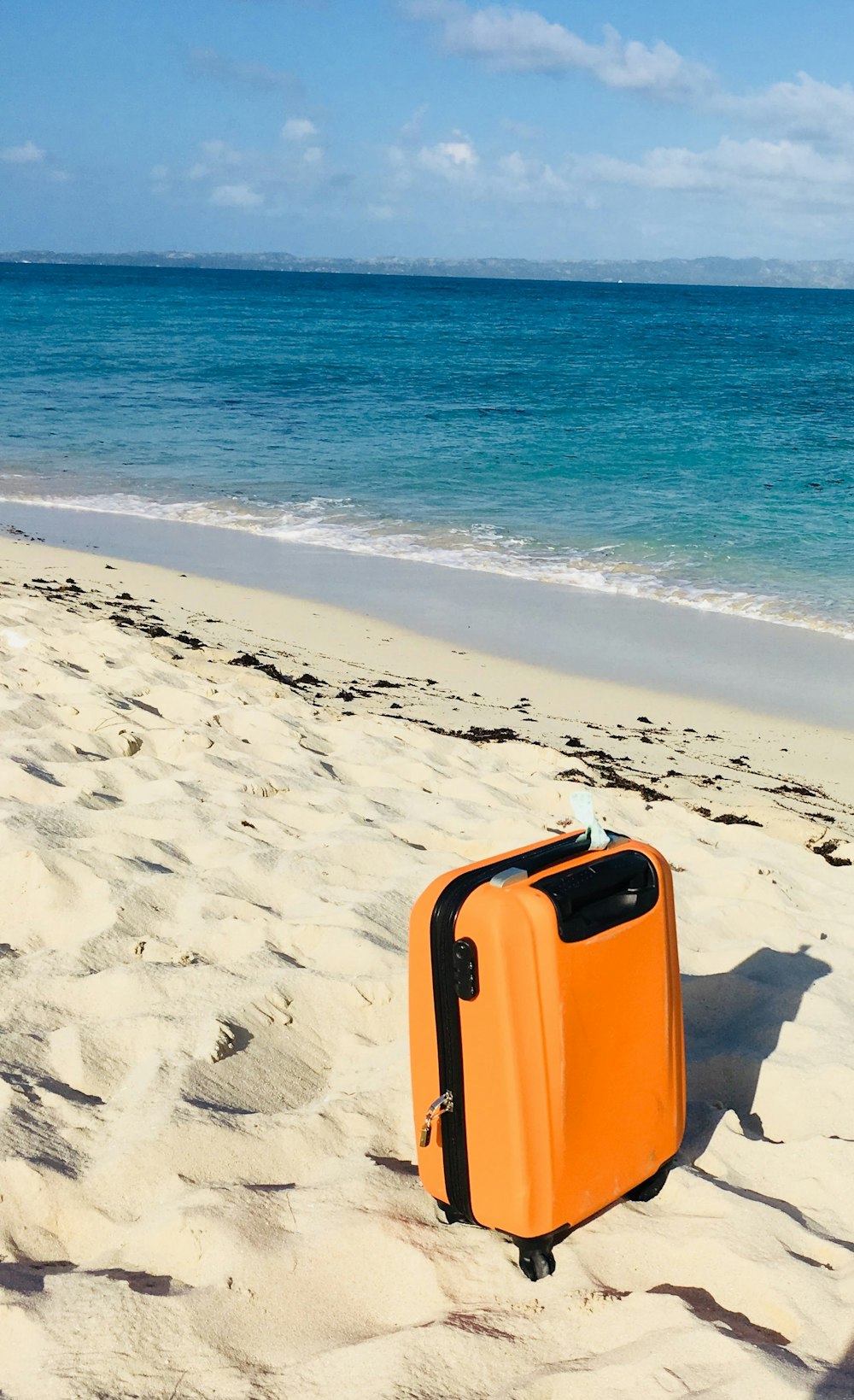 Bolsa de equipaje naranja y blanca en la playa