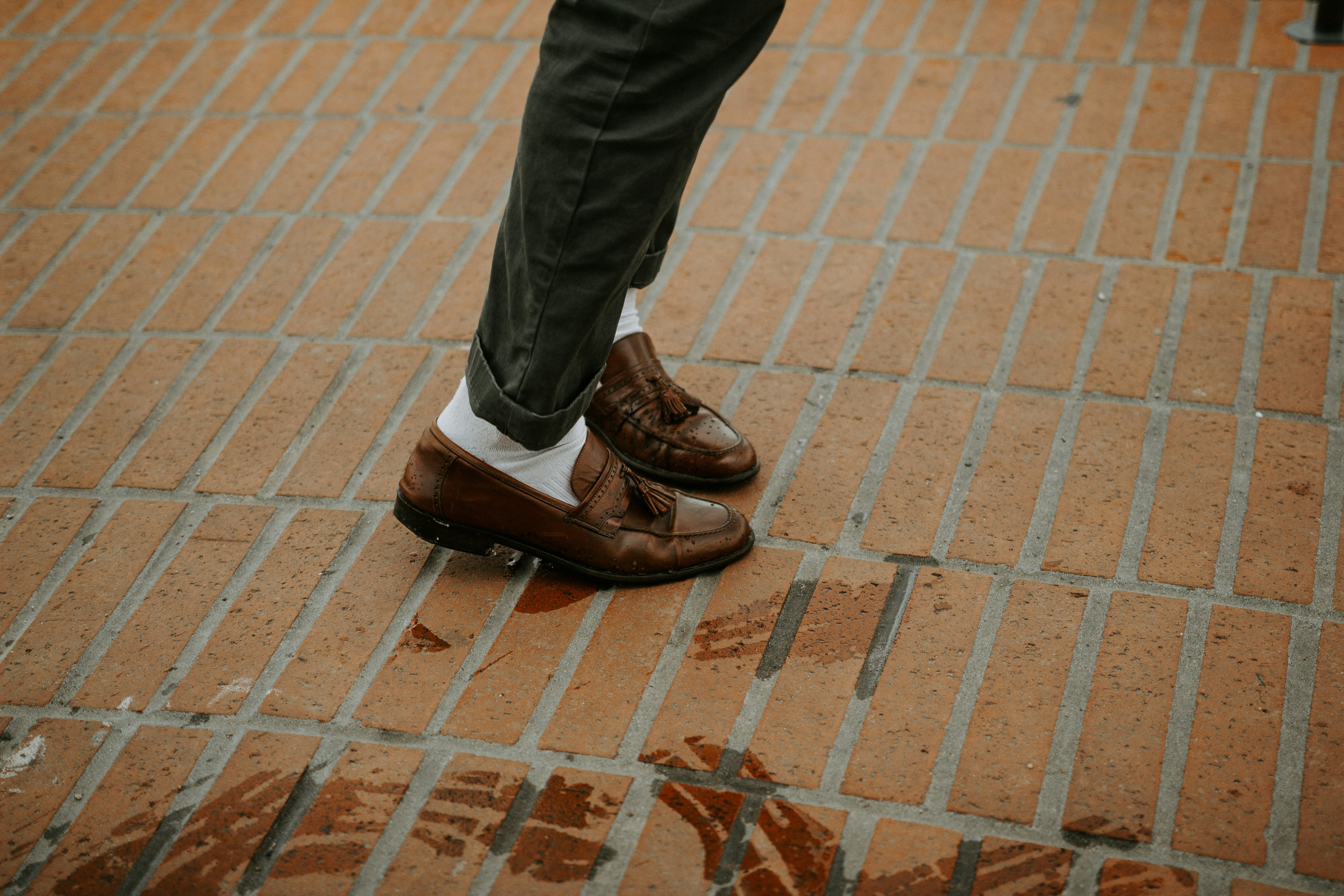person in brown leather shoes standing on brown brick floor