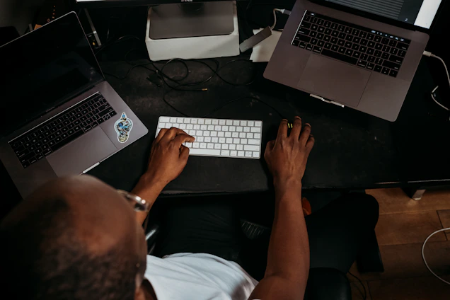 A focused professional typing on a laptop surrounded by stacks of scanned papers and digital devices.