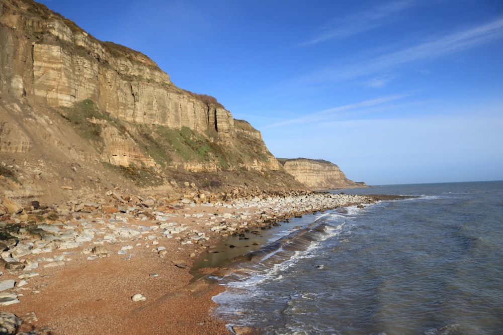 brown rocky mountain beside sea during daytime