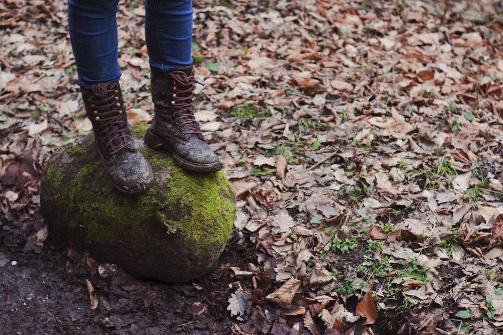 person in blue denim jeans and black and white stripe boots standing on green moss covered