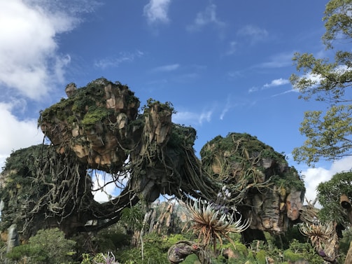 An alien spacecraft hovering above lush forests during the day.