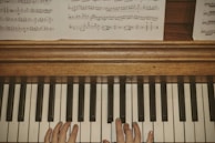 A pair of hands positioned on a piano keyboard, with visible sheet music placed above on a wooden piano surface.