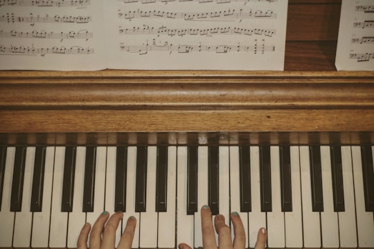 A pair of hands positioned on a piano keyboard, with visible sheet music placed above on a wooden piano surface.