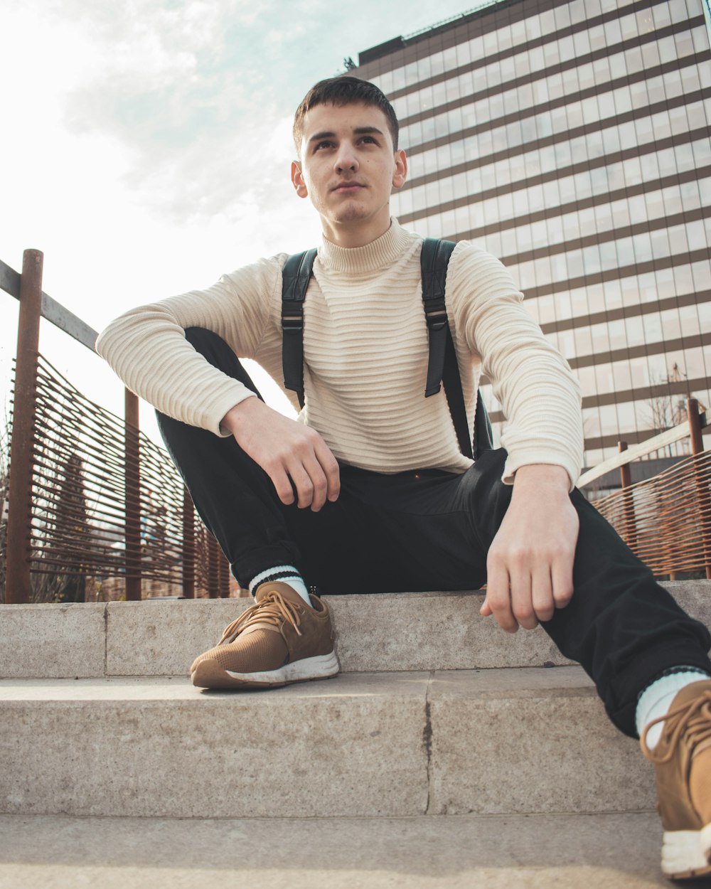 homme en chemise à manches longues rayée blanche et noire et pantalon noir assis sur des escaliers en béton