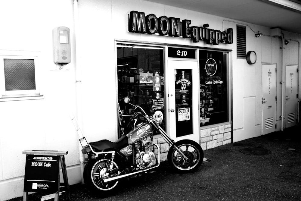 grayscale photo of a motorcycle parked beside the store
