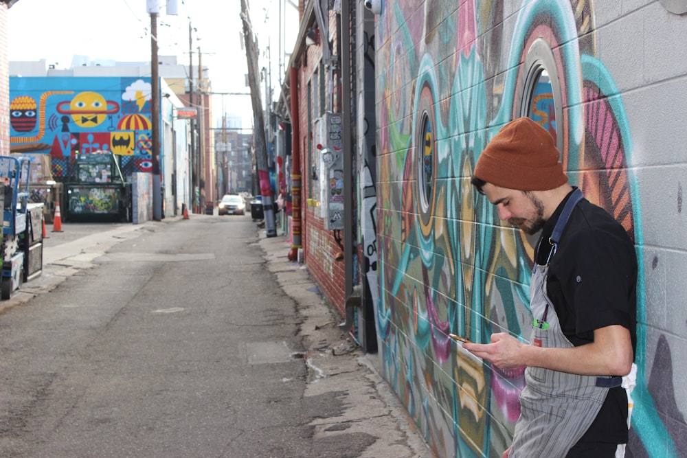 homme en veste noire debout à côté d’un mur de graffitis pendant la journée