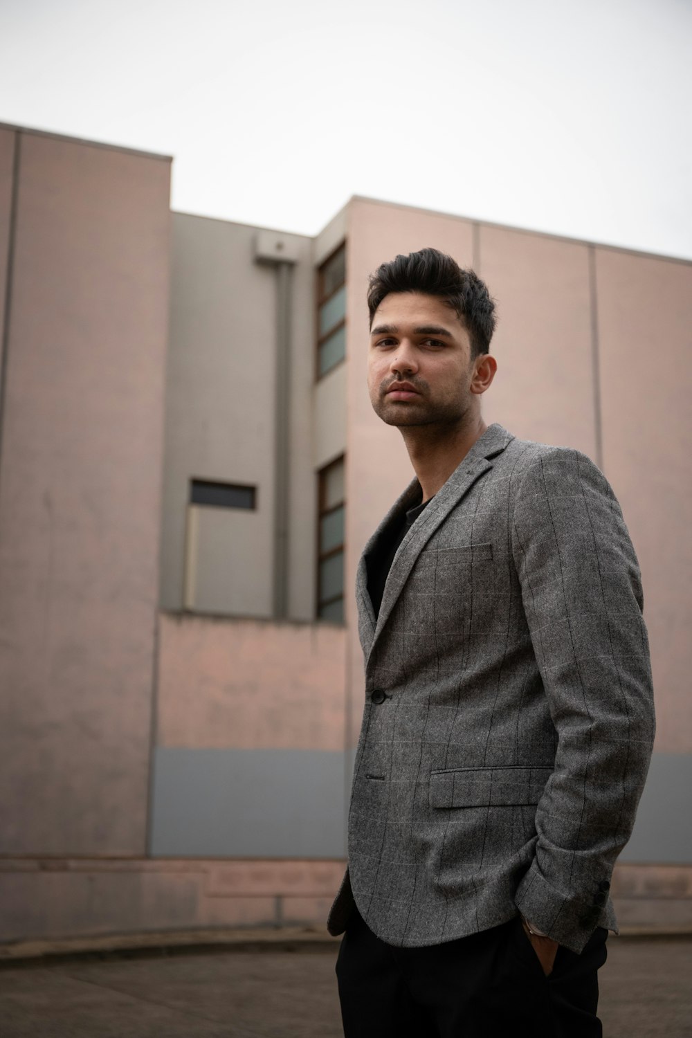 man in gray suit jacket standing near white wall during daytime