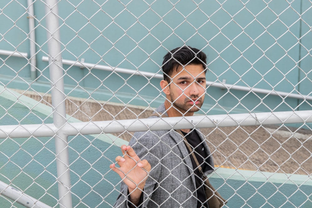 man in gray crew neck shirt leaning on gray metal fence during daytime