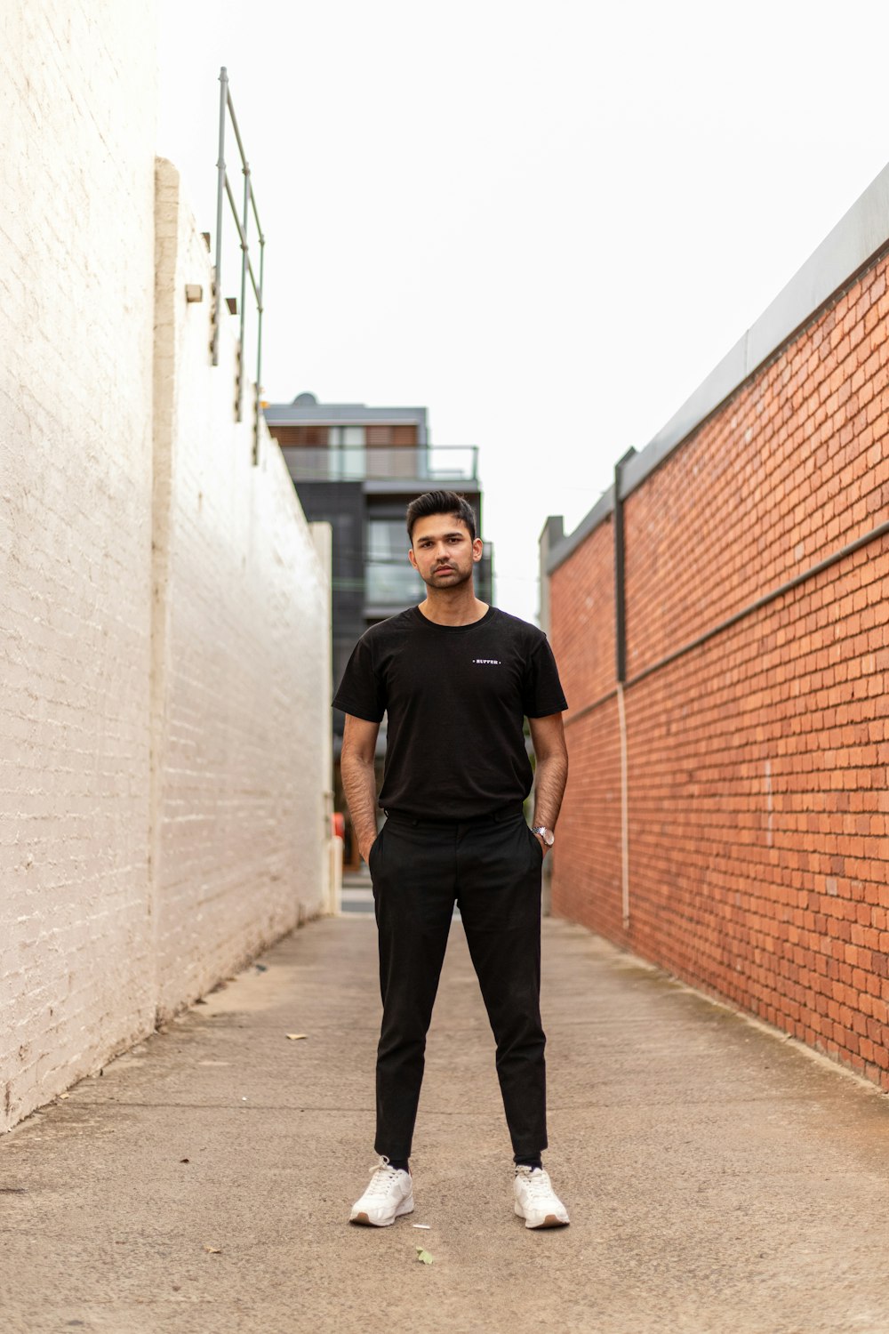 man in black crew neck t-shirt and black pants standing beside brown brick wall during