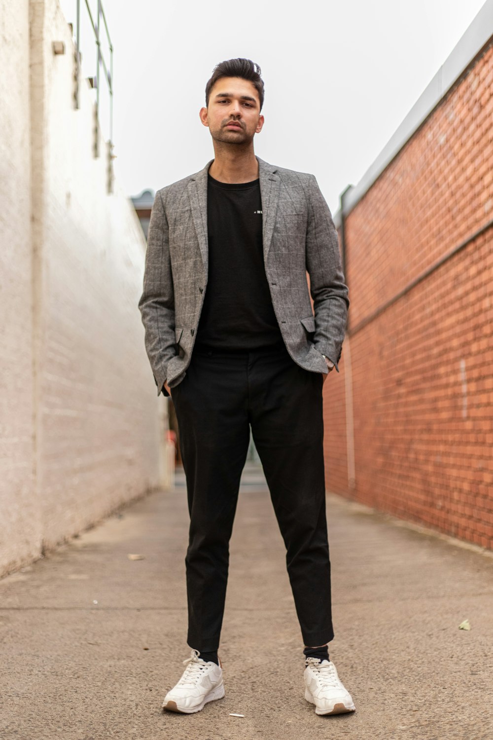 Mann in grauer Anzugjacke und schwarzer Hose, der tagsüber an einer braunen Ziegelwand steht