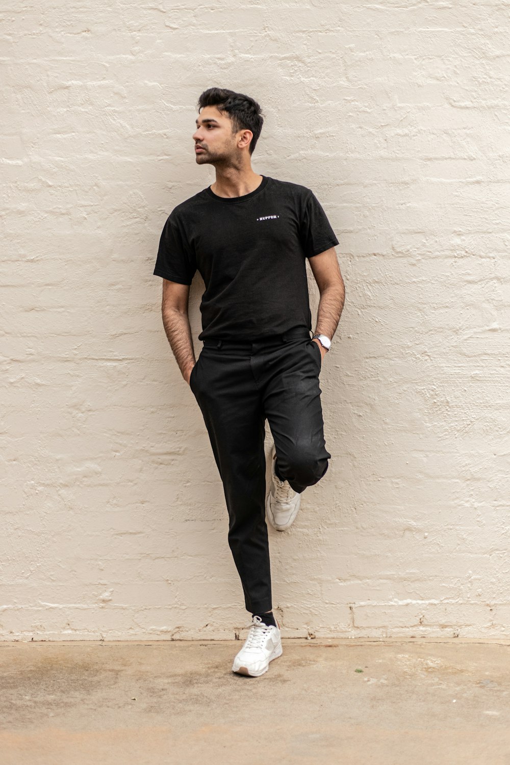 man in black crew neck t-shirt and gray denim jeans leaning on white wall