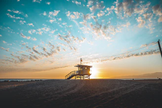 Lifeguard scanning the ocean from a lookout tower with rescue board nearby at sunset on Costa Ballena beach.