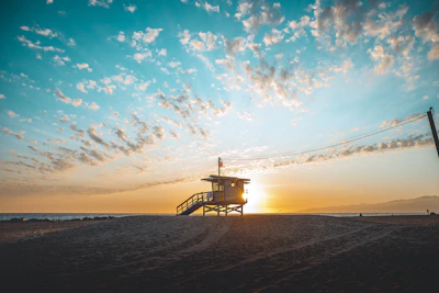 Lifeguard scanning the ocean from a lookout tower with rescue board nearby at sunset on Costa Ballena beach.