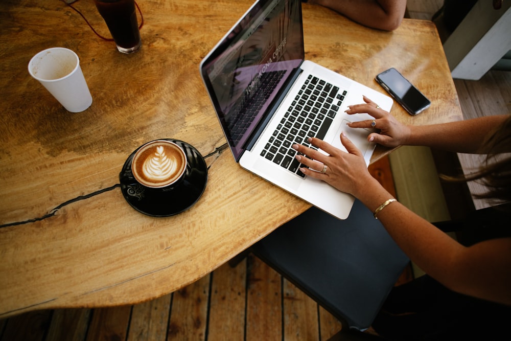 person using macbook pro on brown wooden table