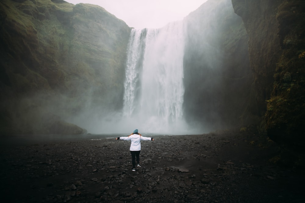 woman in white jacket standing near waterfalls during daytime