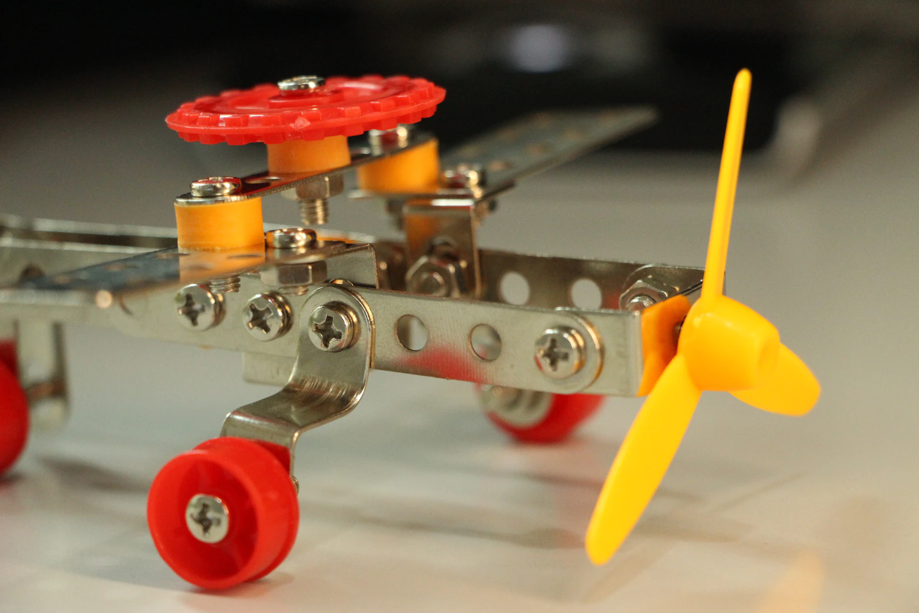 Close-up of a small bolted metal airplane: perforated steel strips, hex nuts, red wheels and a yellow propeller