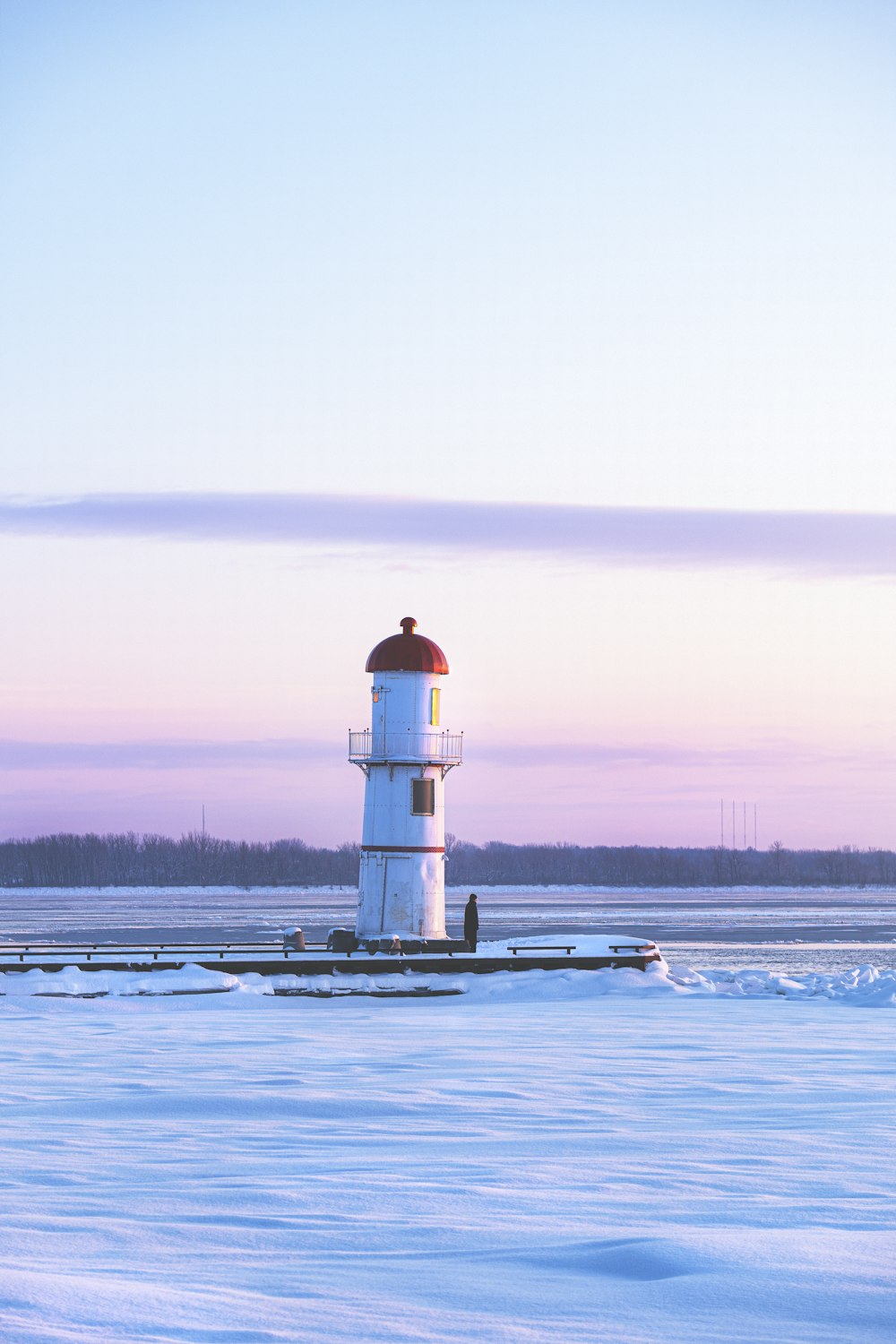 white and black lighthouse on snow covered ground during sunset