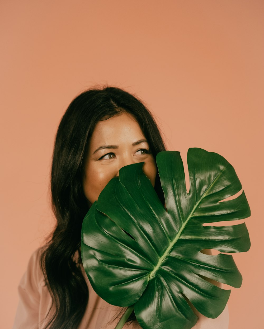 woman in white shirt covering her mouth with green leaf