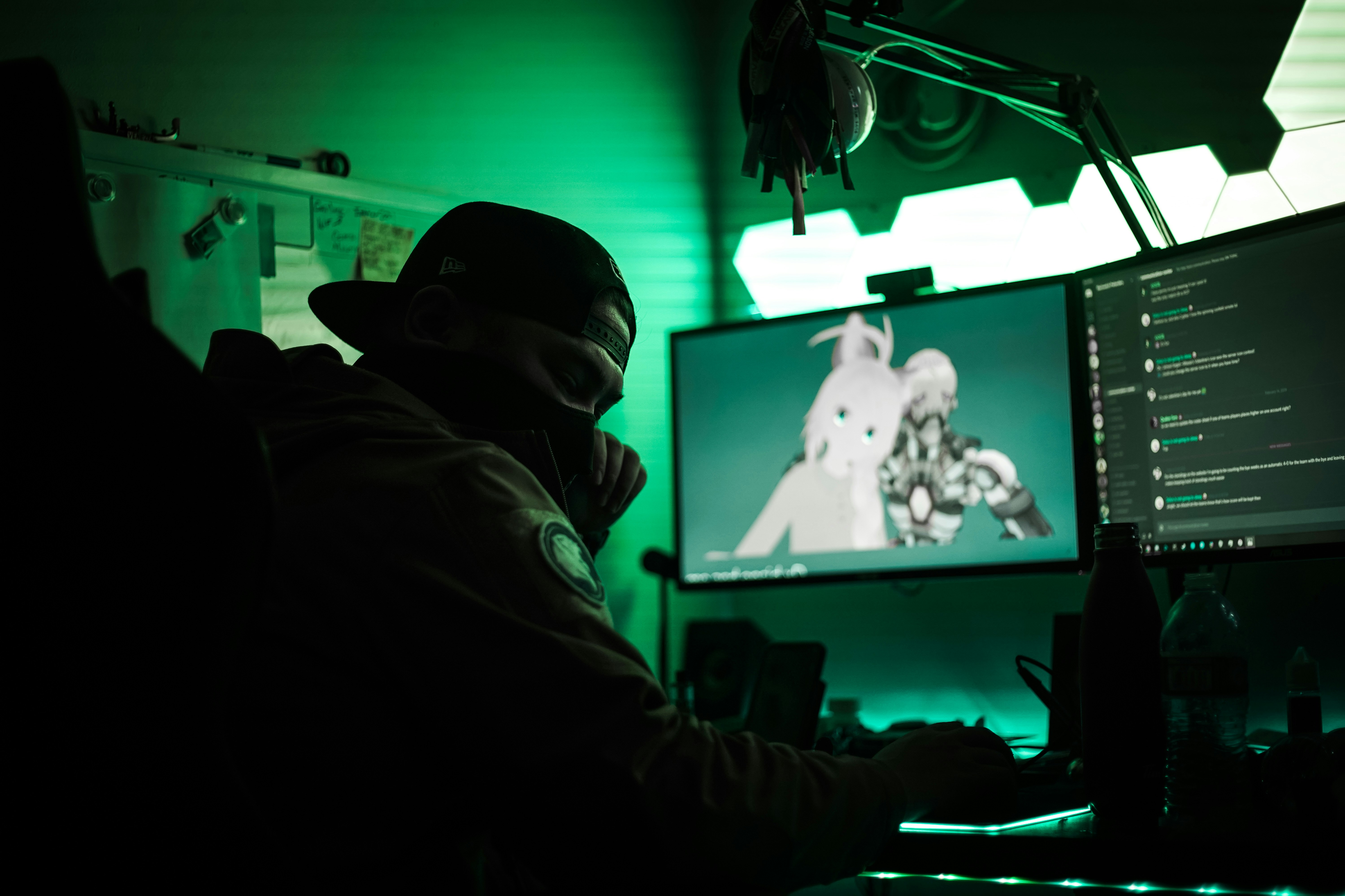 Gamer wearing a mask looks away from glowing computer and light panels.