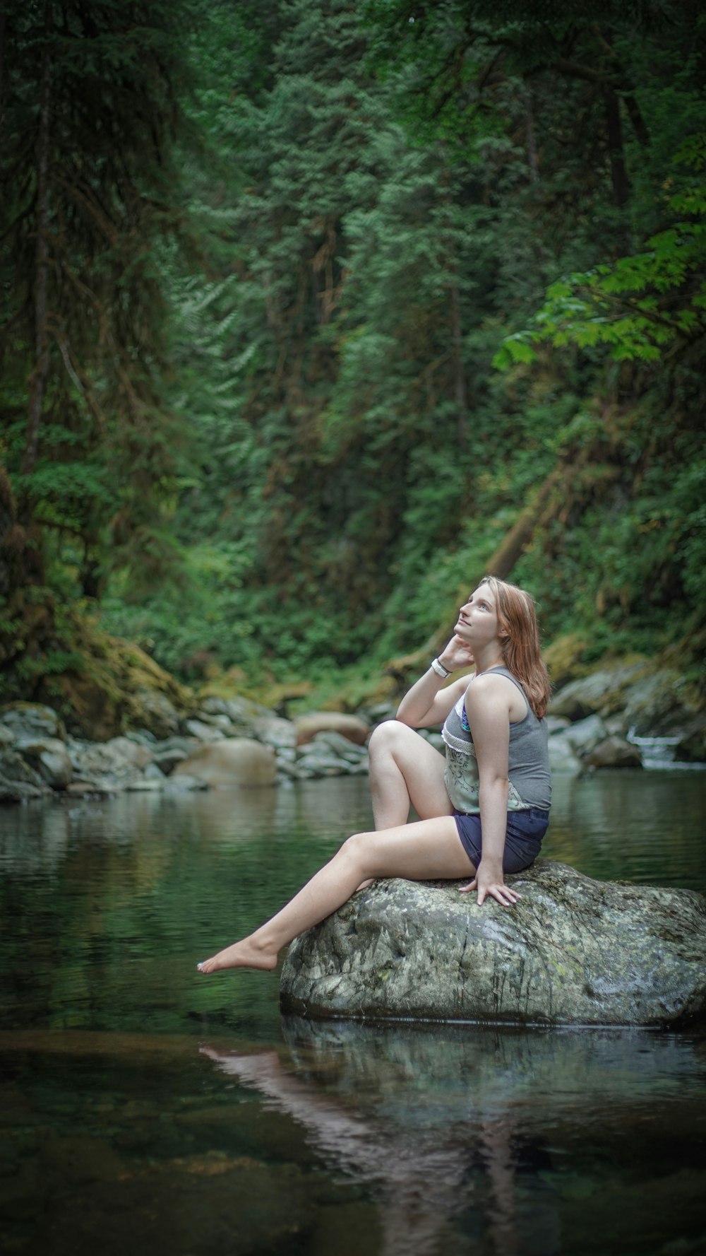 femme en débardeur blanc assise sur un rocher près de la rivière pendant la journée
